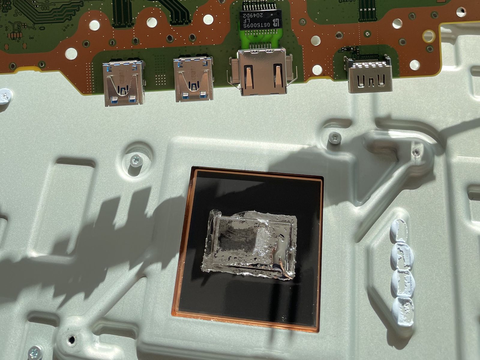 Koelplaat van een PS5 met de resten van het oude vloeibaar metaal, met daarboven de HDMI- en USB-poorten op het moederbord