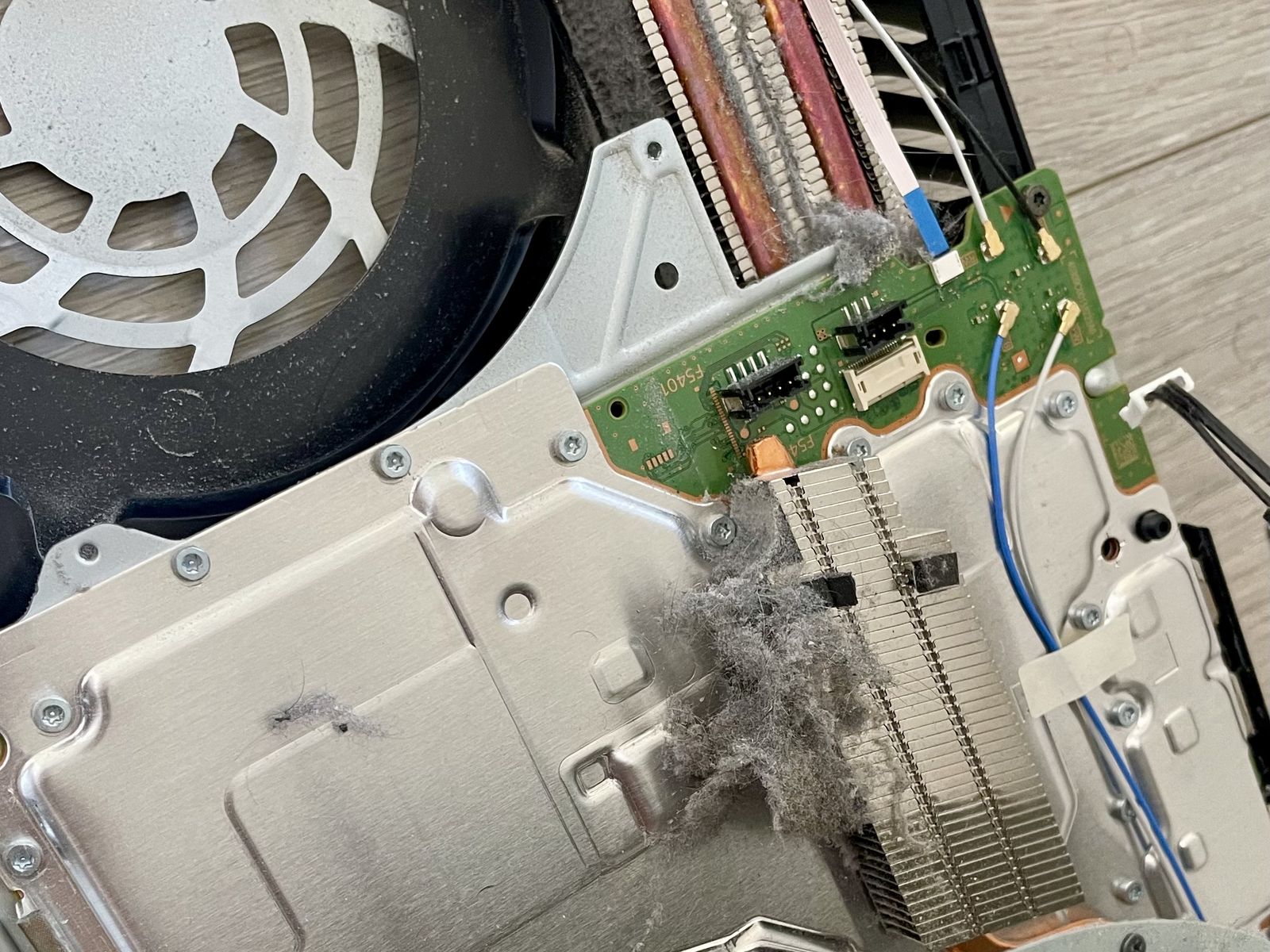 Geopende PS5 met een dikke pluk stof tussen de koelvinnen en stof op de ventilator